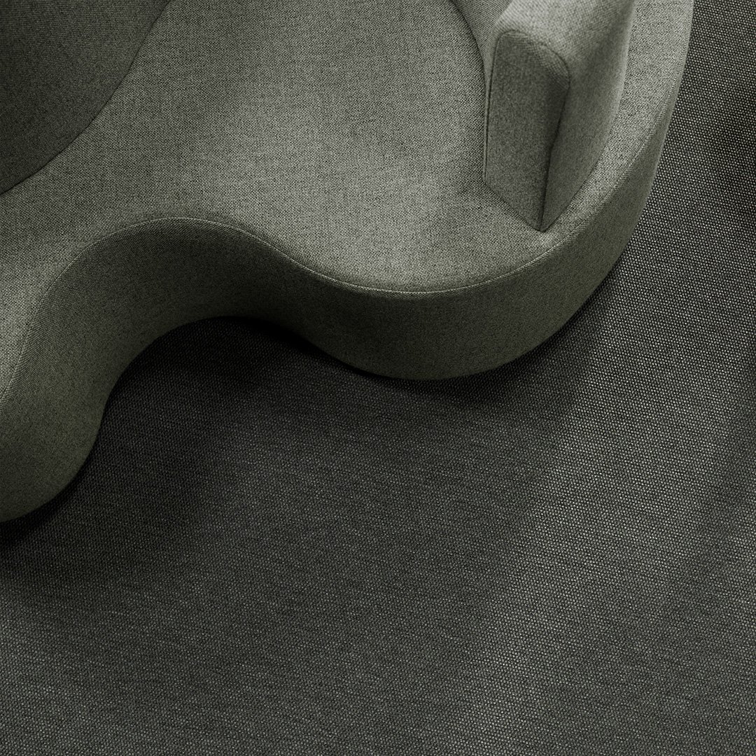 Sisustuskuva, jossa graafinen aaltomuotoinen harmaa sohva vasemmassa yläkulmassa ja tummanharmaa kokolattiamatto.