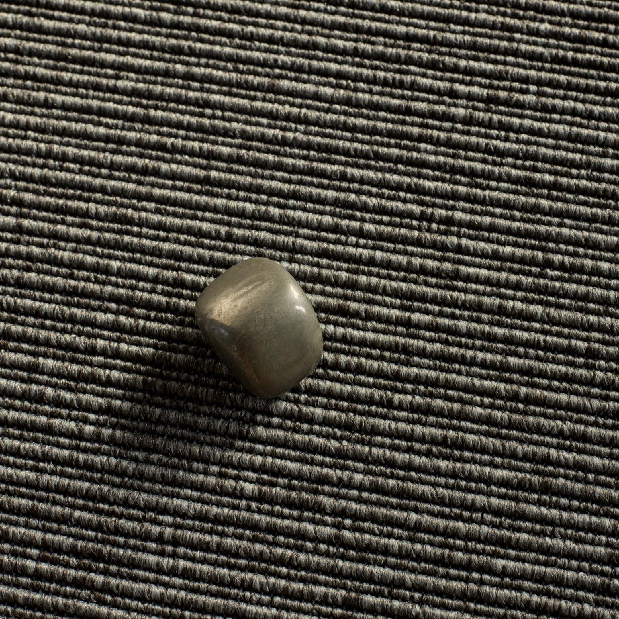 Lähikuva tummanvihreästä tekstiililattiasta, jonka päällä pieni vihreä kivi.
