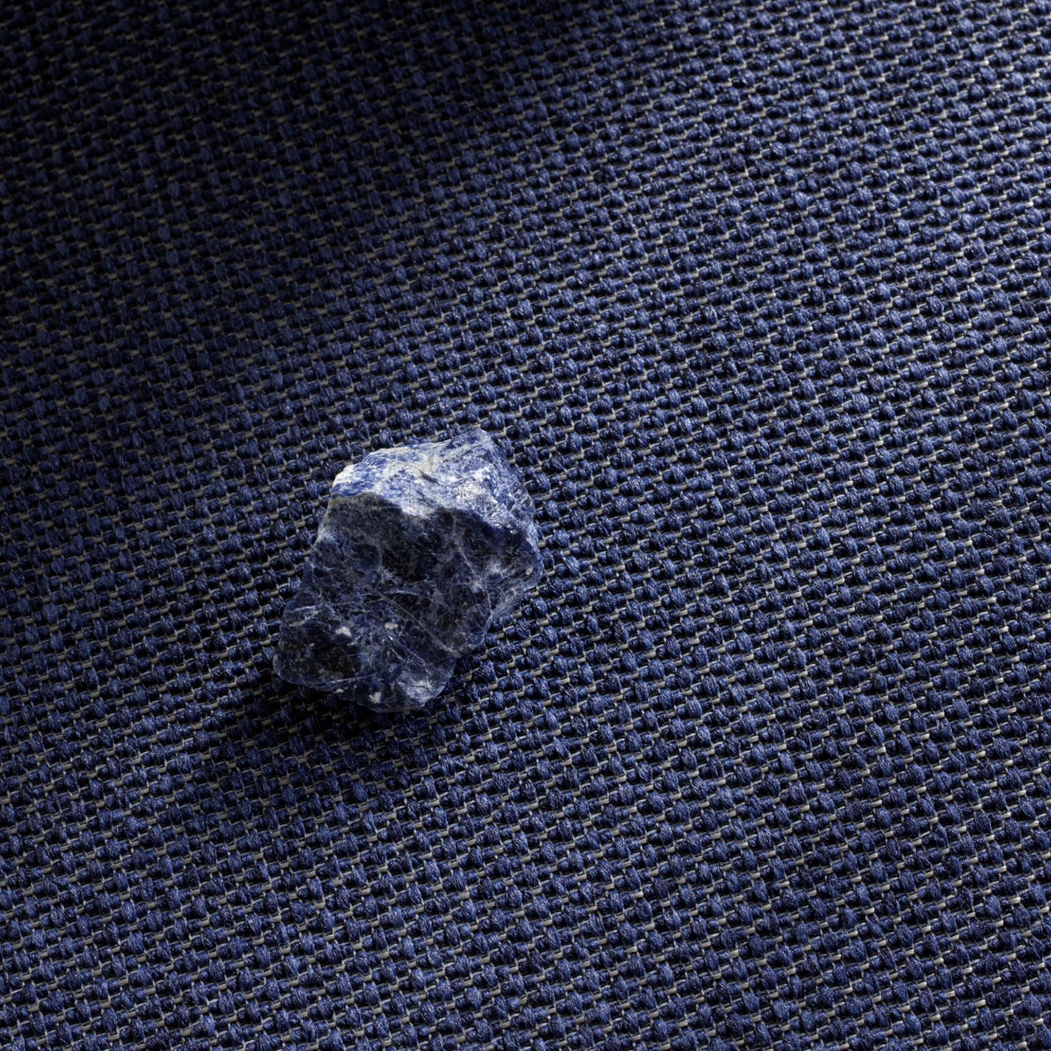 Lähikuva tummansinisestä tekstiiliattiasta, jonka päällä sininen pieni kivi.