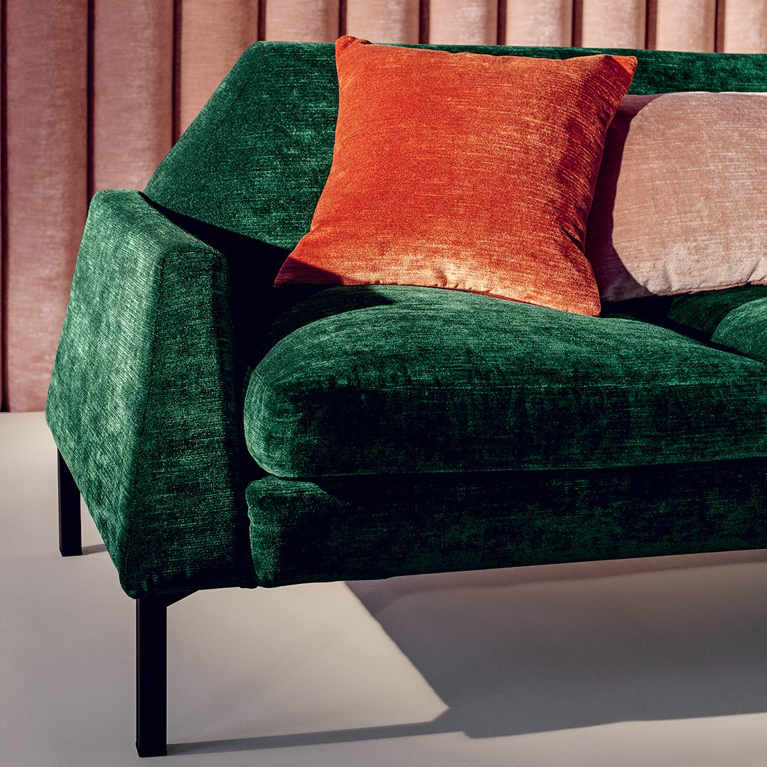 Runsas, tummanvihreällä rouhealla samettikankaalla verhoiltu sohva, jolla vaaleanpunainen ja lohenpunainen samettikankainen tyyny.