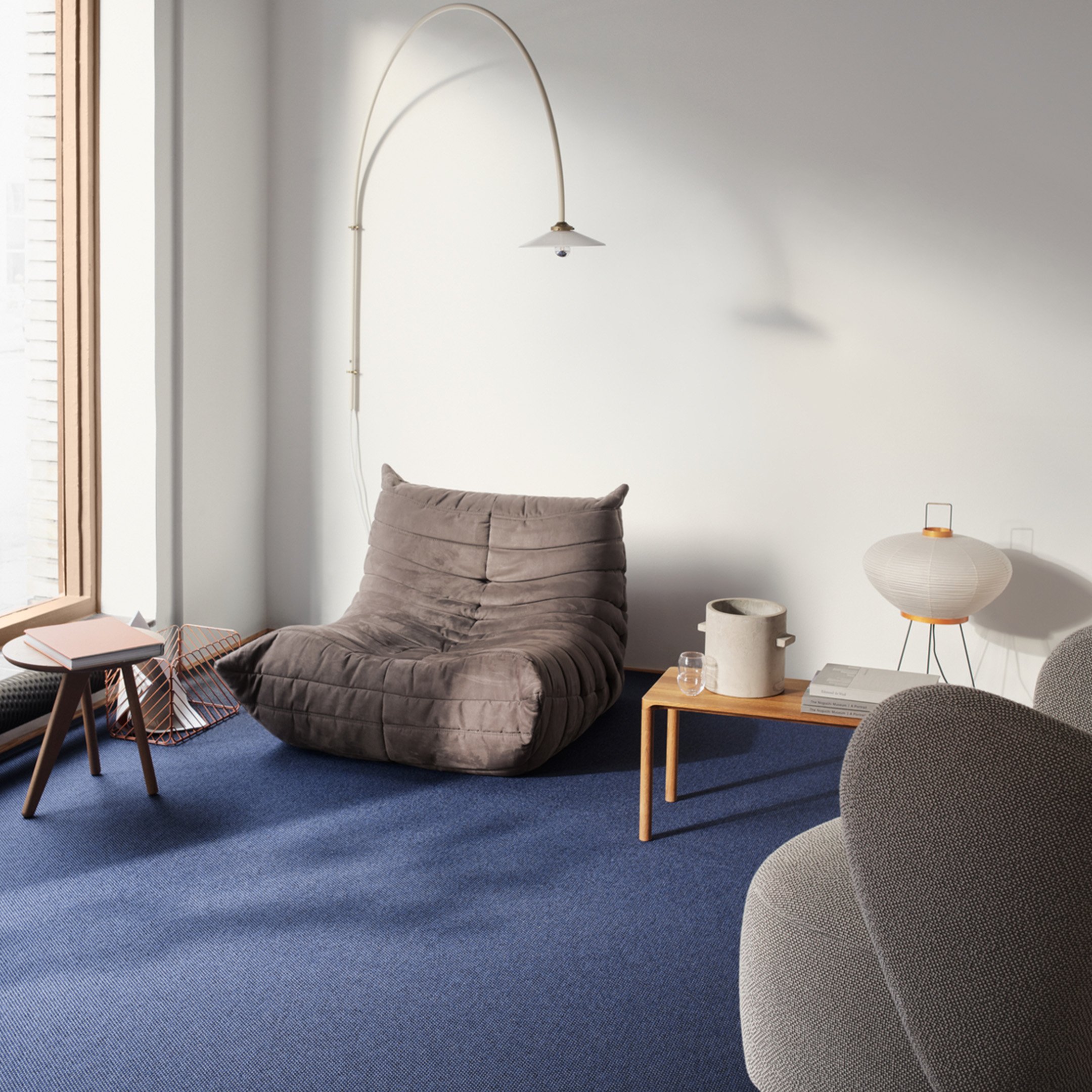 Sininen Ege Carpetsin Eco-tekstiililattia tilassa, jossa on lisäksi Ligne Rosetin klassikko Togo-sohva, jakkara, sivupöytä, sekä kaareva seinälamppu.
