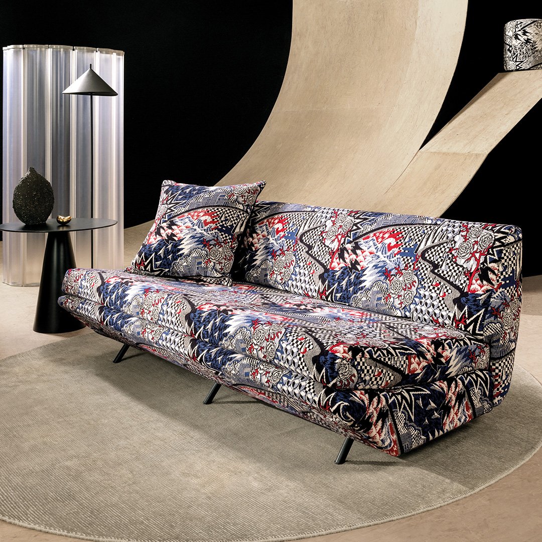 Kuva sohvasta, jossa näyttävä graafinen värikäs verhoilu, jossa ruusuja, siksak-kuvioita ja kohtia, jotka näyttävät vuorimaisemilta.